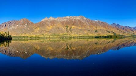 Mountain peaks and forest reflect in a calm lake in Yukon, Canada.