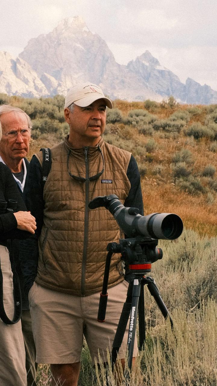 Alt text A small group of people watches wildlife through a spotting scope in an open sagebrush landscape with mountains in the distance.