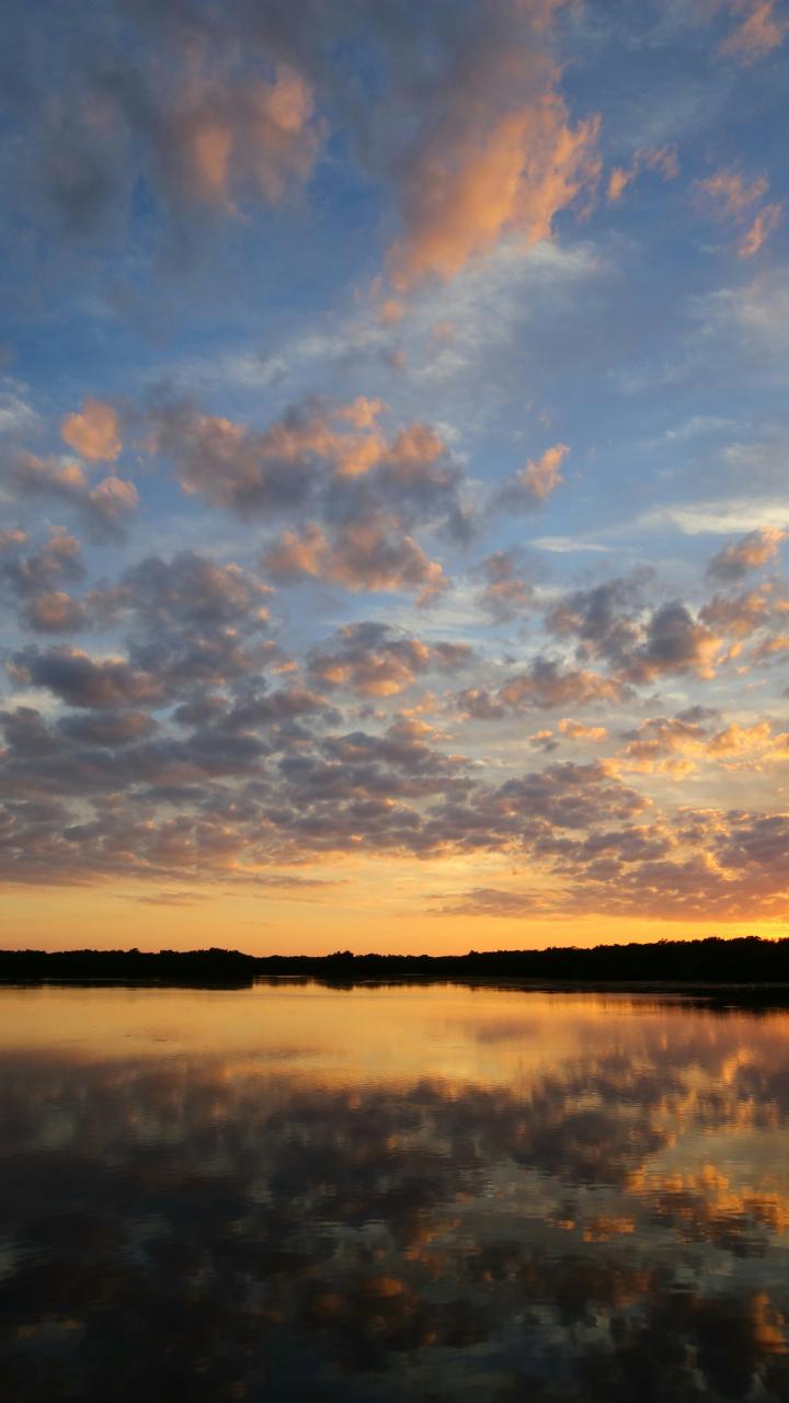 Sunset over Perico Island, Florida, reflected on calm water beneath scattered clouds.